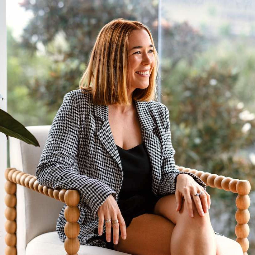 Kate Holland Radar Founder and WellBeing editor sitting on a chair indoors with a blurred outdoor background