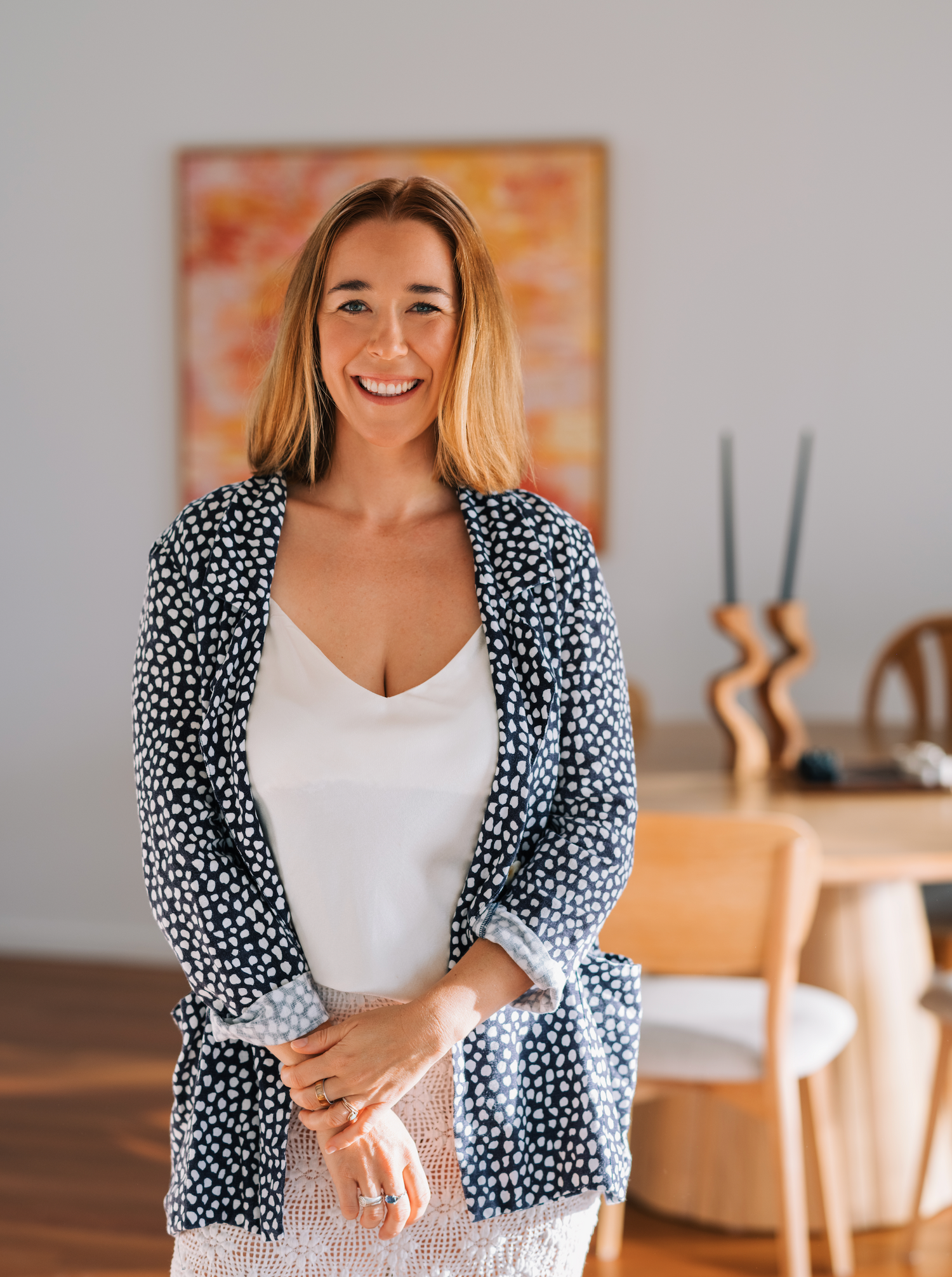 Kate Holland standing in a room with a painting on the wall and a table in the background